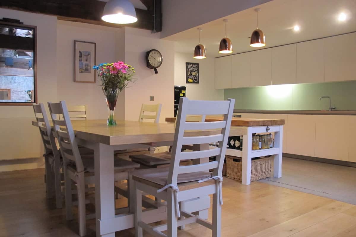 Un coin repas avec une table et des chaises en bois, un vase avec des fleurs, une horloge et des lampes suspendues.