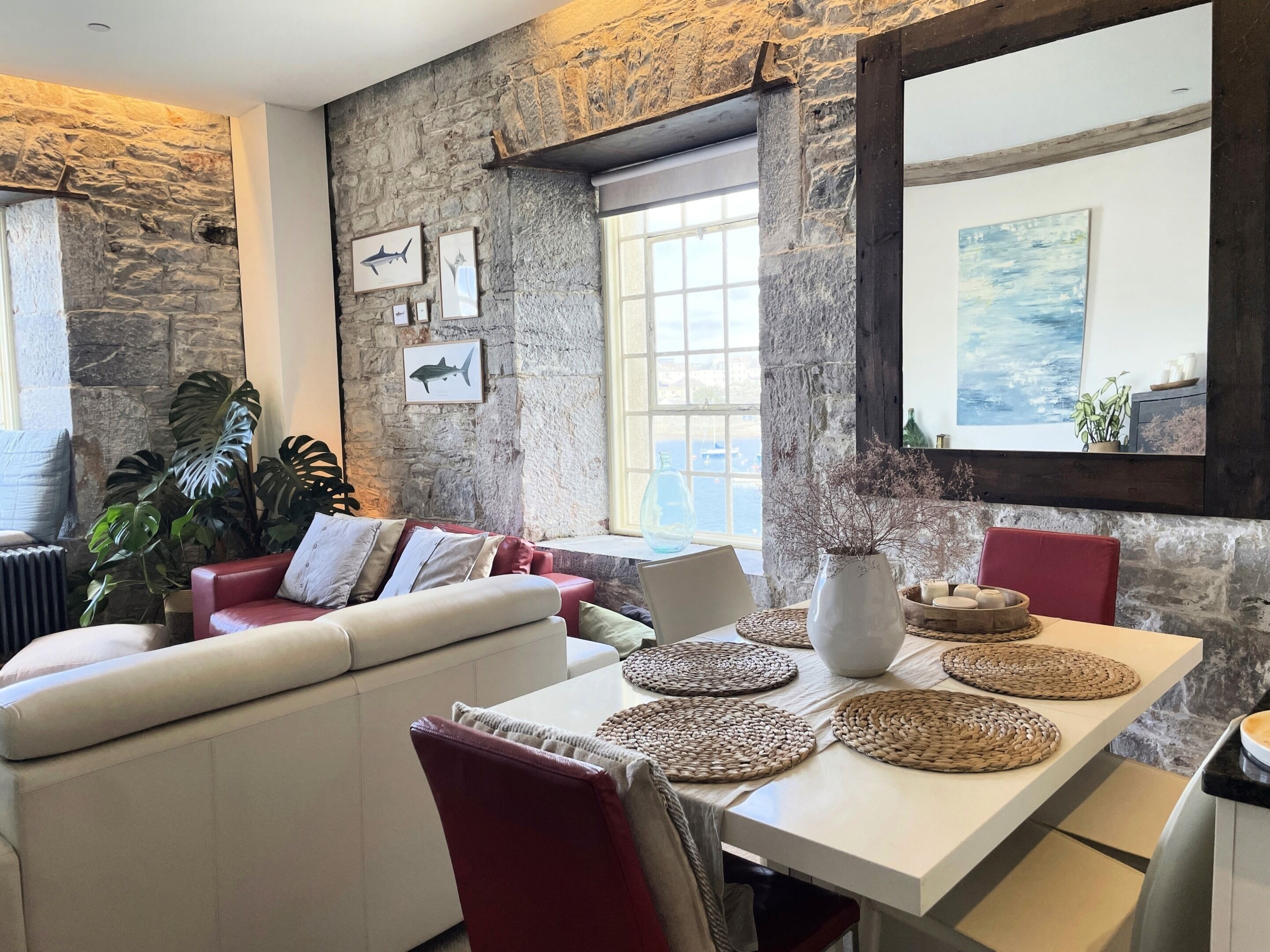 A cozy living room with a stone wall, a white sofa, a dining table with woven placemats, and framed artwork.