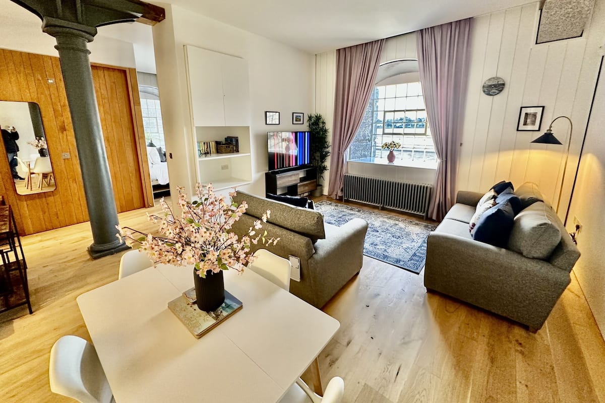 Un salon moderne comprenant une table à manger, deux canapés, un téléviseur et une grande fenêtre avec des rideaux.