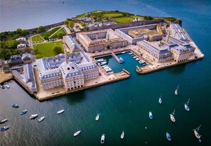 Luchtbeeld van een historische haven met een groot complex, een jachthaven vol boten en een klein eiland met begroeiing en gebouwen.