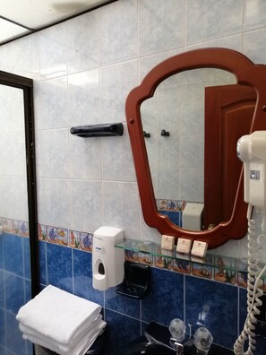 Une salle de bain équipée d’un sèche-mains, d’un distributeur de savon, d’une étagère en verre où sont rangés les articles de toilette et d’un miroir avec un cadre en bois.
