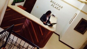 A reception desk with a person working on a laptop, a sign reading "BOLIVAR PLAZA", and a staircase with a railing. - Hotel Bolivar Plaza Manizales (Manizales)