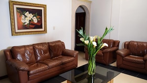 A living room with a brown leather sofa, a glass coffee table, and a vase with white flowers. - Hotel Bolivar Plaza Manizales (Manizales)