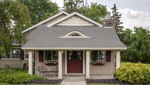 A two-story house with a red front door, a small porch with a bench, and a number "115" on the door. - White Springs Manor a Belhurst Property (Geneva)