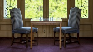 A room with two chairs and a table, a large arched window with stained glass, and a view of greenery outside. - White Springs Manor a Belhurst Property (Geneva)