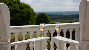 Two white chairs with white railings, each holding a glass of wine. - White Springs Manor a Belhurst Property (Geneva)
