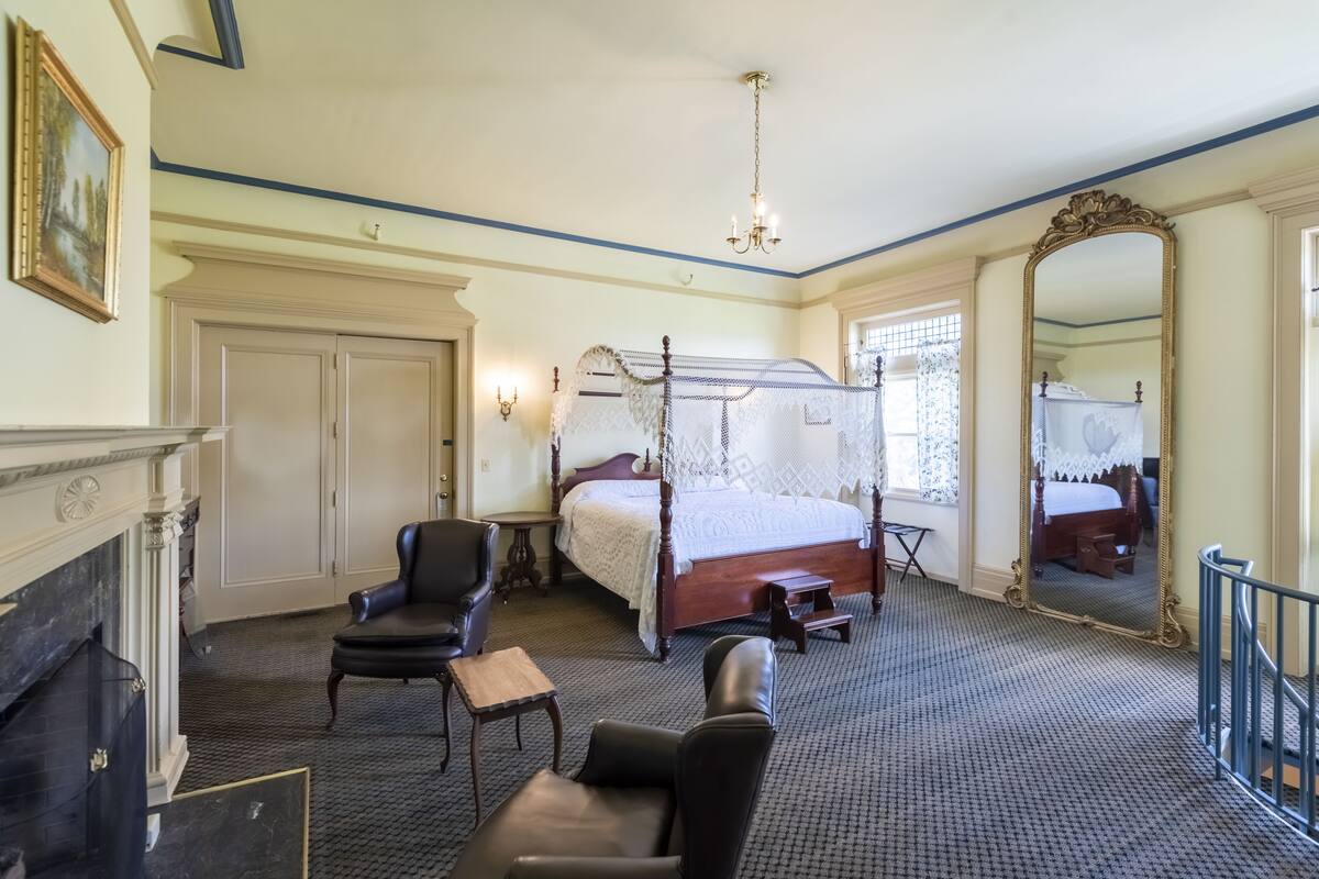 Ein Schlafzimmer mit einem Himmelbett, einem Kamin, einem großen Spiegel und einer Chandelier.