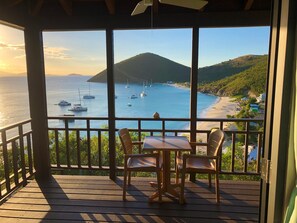 Eine Holzterrasse mit Tisch und Stühlen, mit Blick auf eine Bucht, in der Boote und ein Strand liegen.