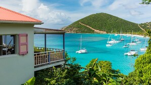 Ein Küstengebäude mit Balkon, das auf türkisfarbenes Wasser und einen Hafen mit Segelbooten blickt.