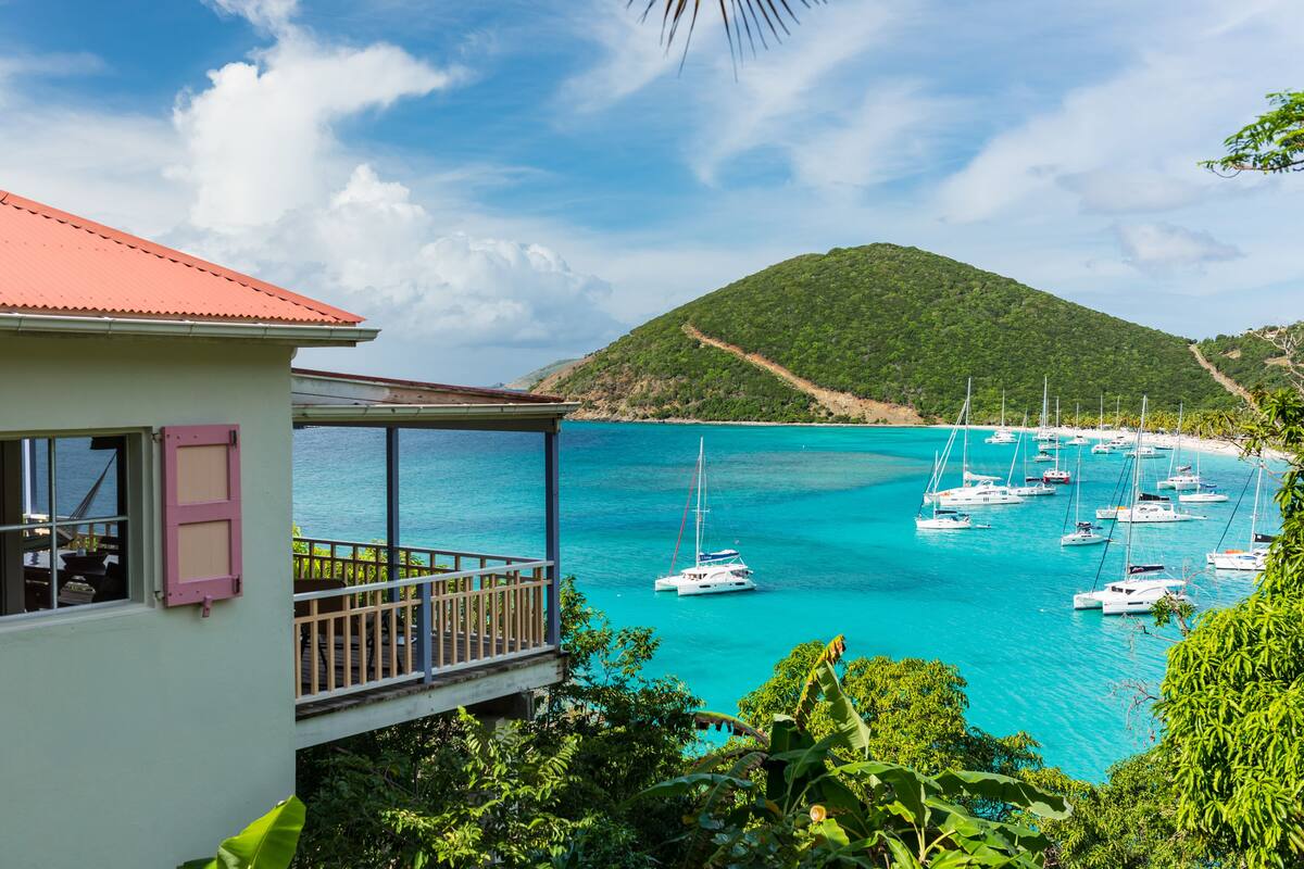 A coastal building with a balcony overlooking turquoise waters and a marina with sailboats.