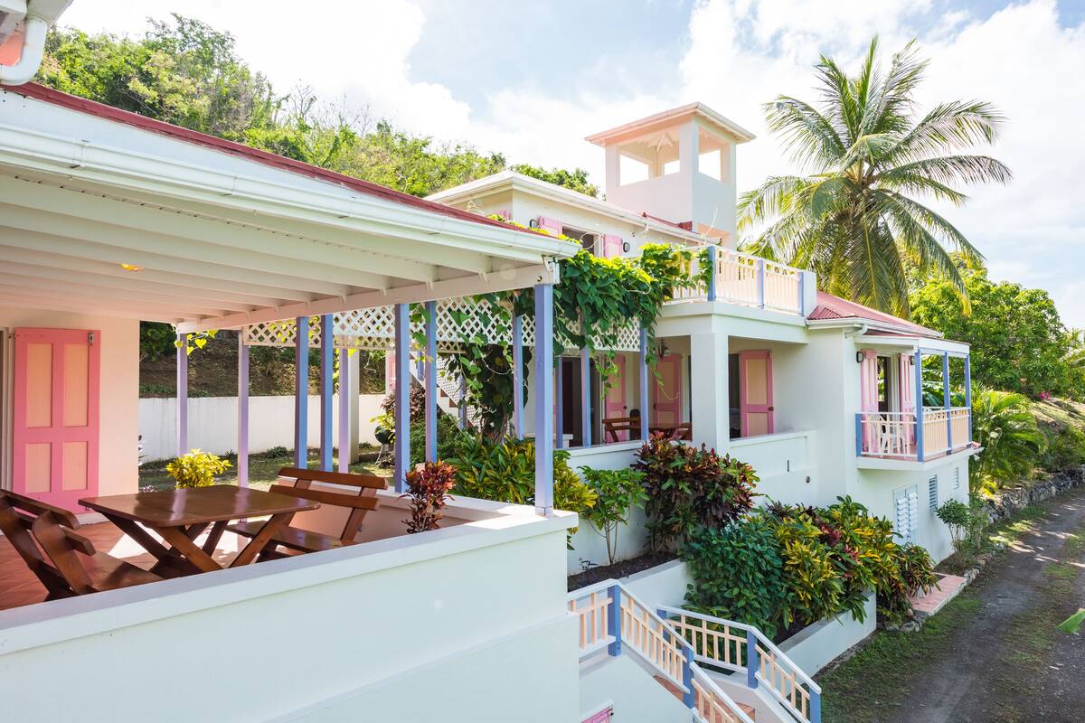 A two-story house with a covered patio, a balcony, and lush greenery.