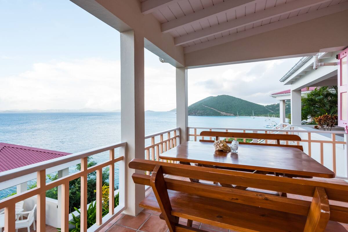A wooden table with benches on a balcony overlooking a beach and ocean.