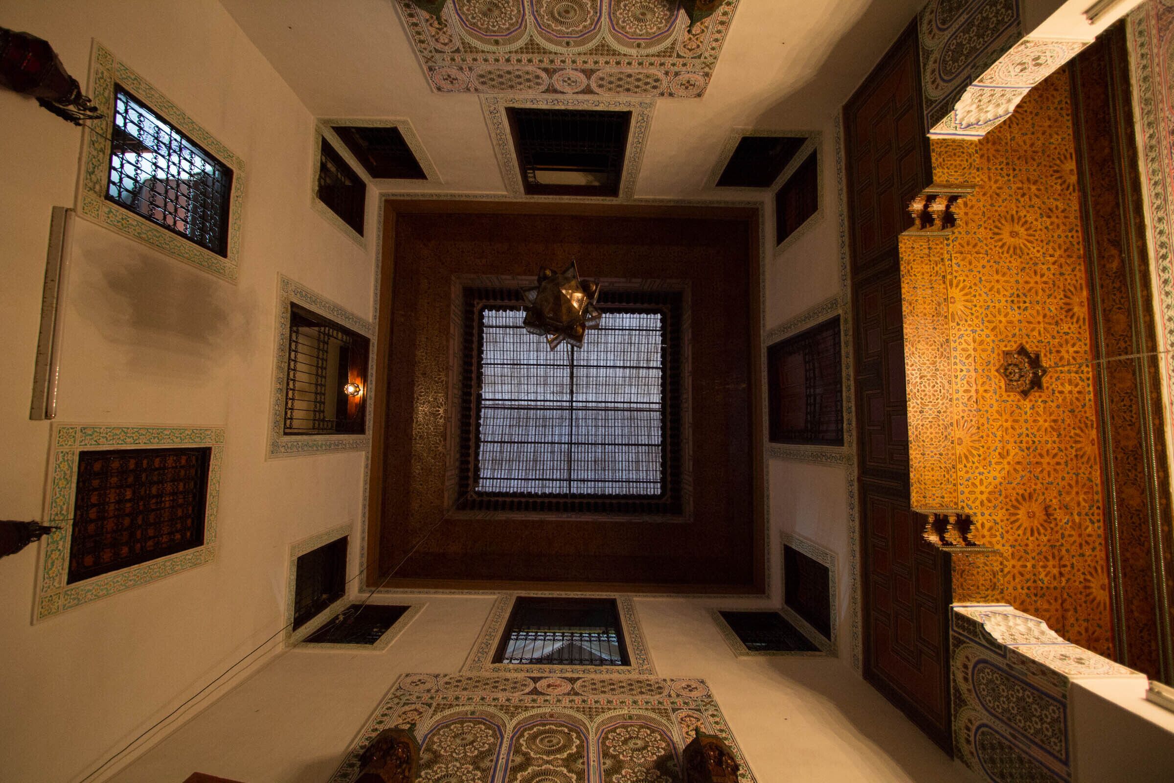 A room with a large central window, decorative ceiling patterns, and ornate wall tiles.