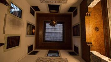 A room with a large central window, decorative ceiling patterns, and ornate wall tiles.