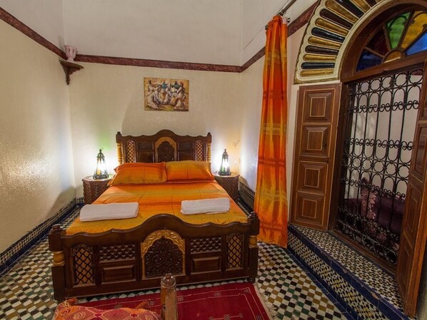 A traditional Moroccan room with a wooden bed, patterned floor, and a decorative door.