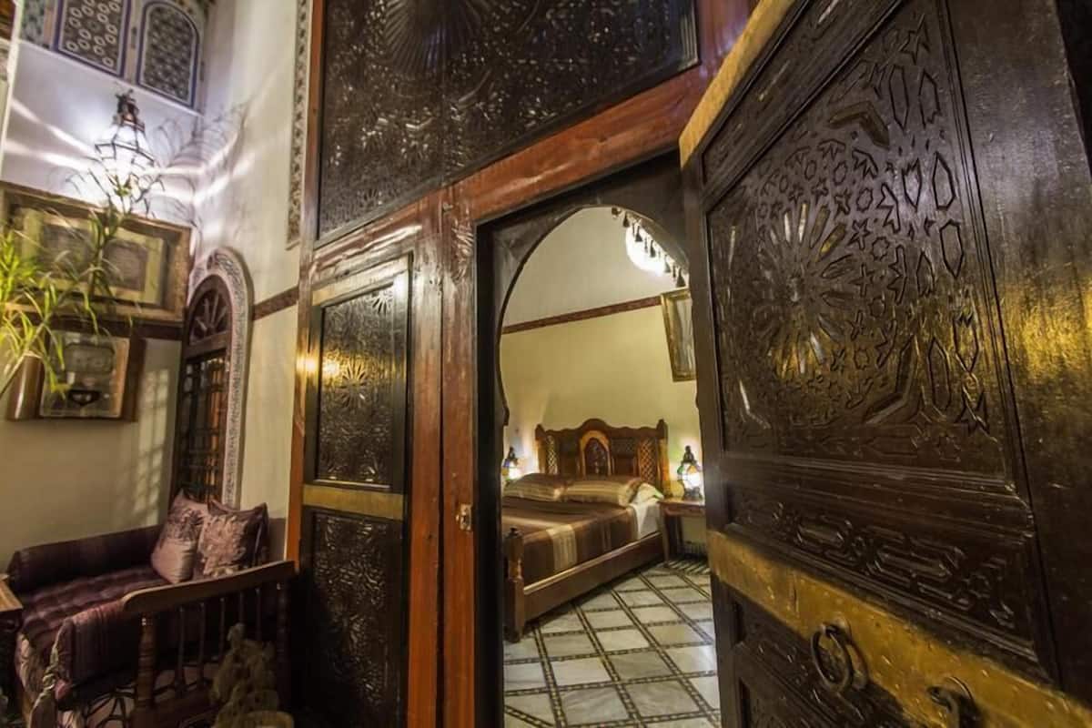 Une pièce traditionnelle marocaine avec une porte en bois, un lit et un petit coin salon.