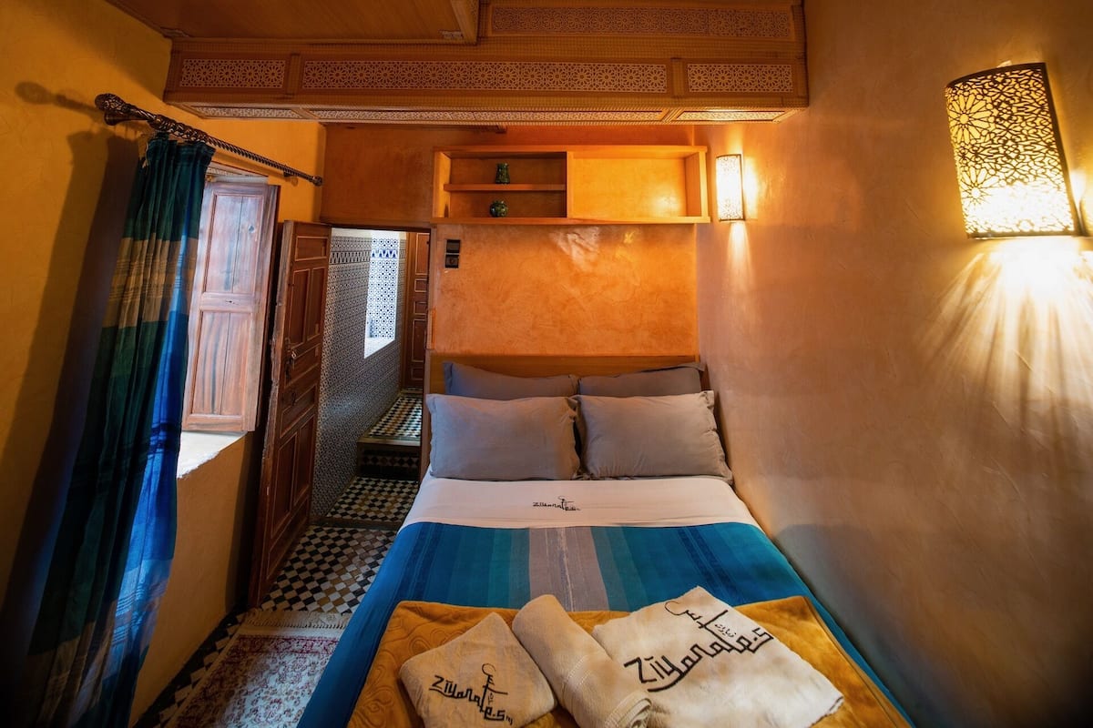 Une petite pièce comprenant un lit, une étagère et un appliques mural décoratif.