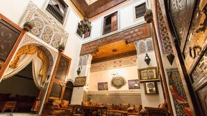 A traditional Moroccan interior with ornate tile work, a seating area with cushions, and a decorative archway. - Riad Meski (Fes)