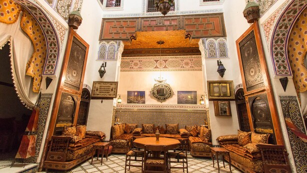 A traditional Moroccan interior with ornate arches, a central seating area with cushions, and a tiled floor. - Riad Meski (Fes)