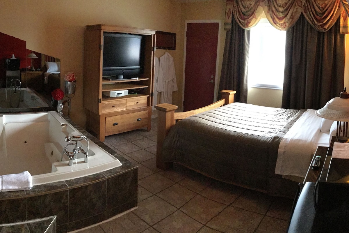 Une chambre d’hôtel équipée d’une grande baignoire, d’un lit, d’une télévision et d’une coiffeuse avec un miroir.