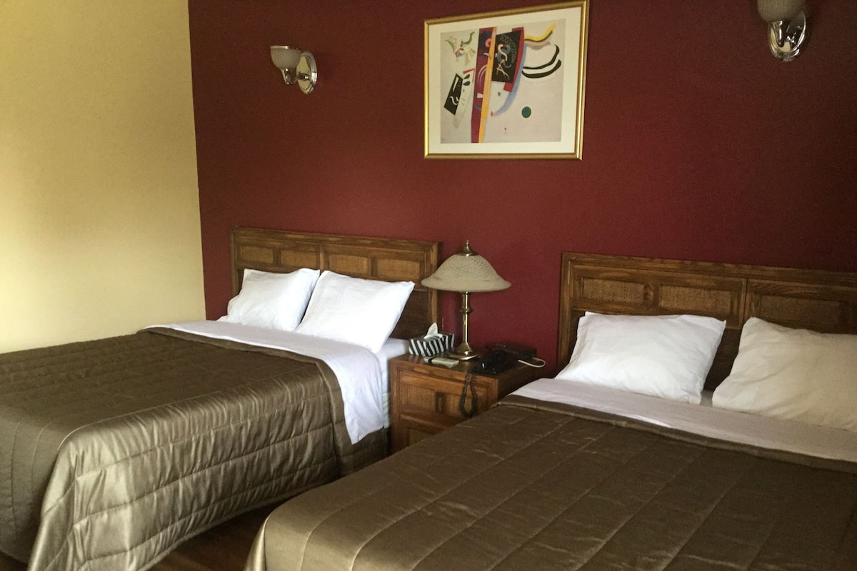 Une chambre d’hôtel avec deux lits, une tête de lit en bois, une table de chevet avec une lampe et un tableau abstrait encadré accroché au mur.