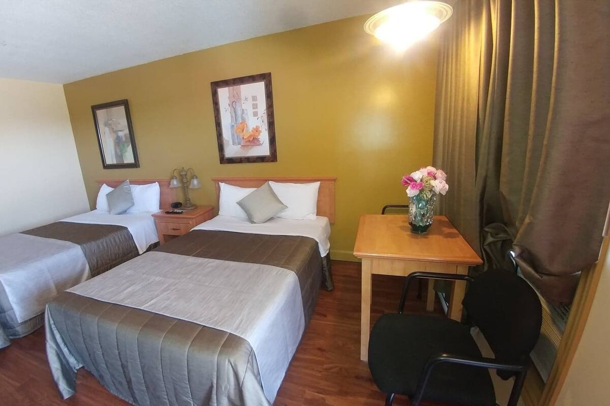 Une chambre d’hôtel avec deux lits, un bureau, une chaise et un vase de fleurs.