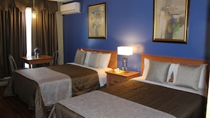 A hotel room with two beds, a nightstand with a lamp, a chair, and two framed artworks on the wall. - Hotel Motel Hospitalité (Levis)