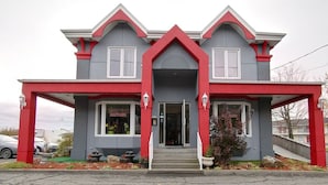 A two-story building with a red and grey facade, a central entrance with steps, and two visible windows on the ground floor. - Hotel Motel Hospitalité (Levis)