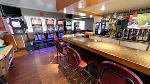A bar area with multiple gaming machines, a counter with stools, and a television screen. - Hotel Motel Hospitalité (Levis)
