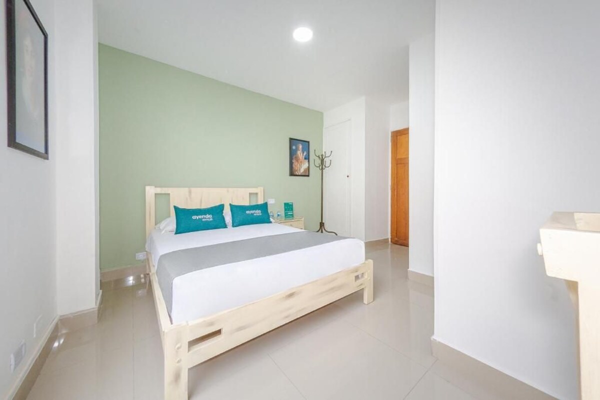 A bedroom with a wooden bed, a nightstand, a lamp, and a door leading to another room.