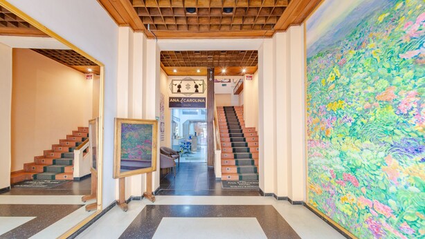 A hotel lobby with a star-patterned floor, a staircase, and a large floral mural. - Ayenda Ana Carolina (Manizales)