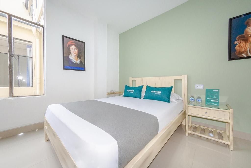 A hotel room with a bed, a nightstand, a window, and two wall-mounted pictures.