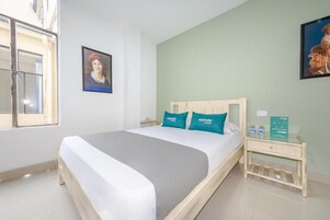 A hotel room with a bed, a nightstand, a window, and two wall-mounted pictures.