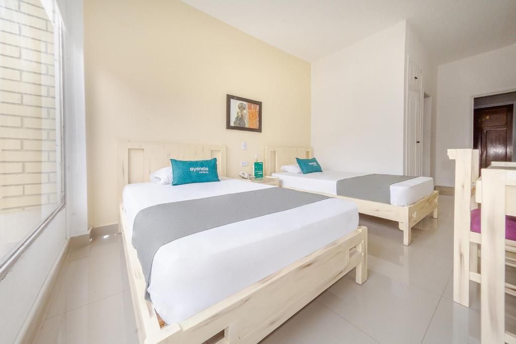A hotel room with two beds, each with a pillow and a bedside table.