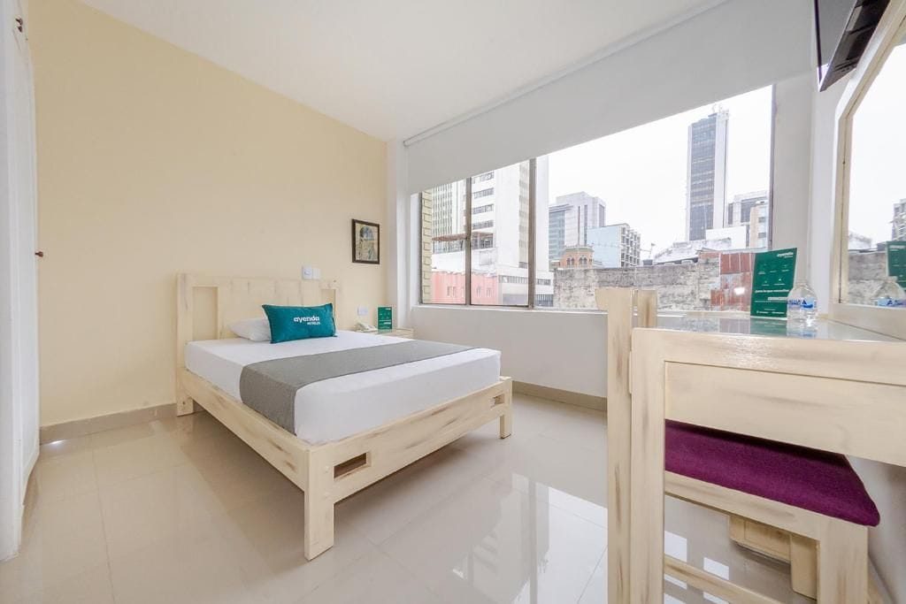 Una habitación de hotel con una cama, un ventanal con vista a la ciudad y un escritorio con una silla.
