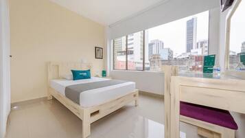 Una habitación de hotel con una cama, un ventanal con vista a la ciudad y un escritorio con una silla.