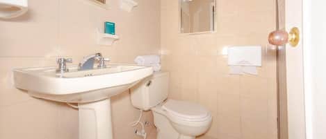Un baño con lavamanos blanco, inodoro y espejo sobre el lavamanos.