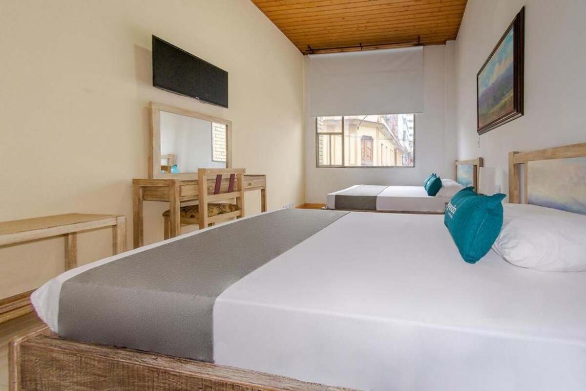 A hotel room with a large bed, a desk, a chair, and a window.