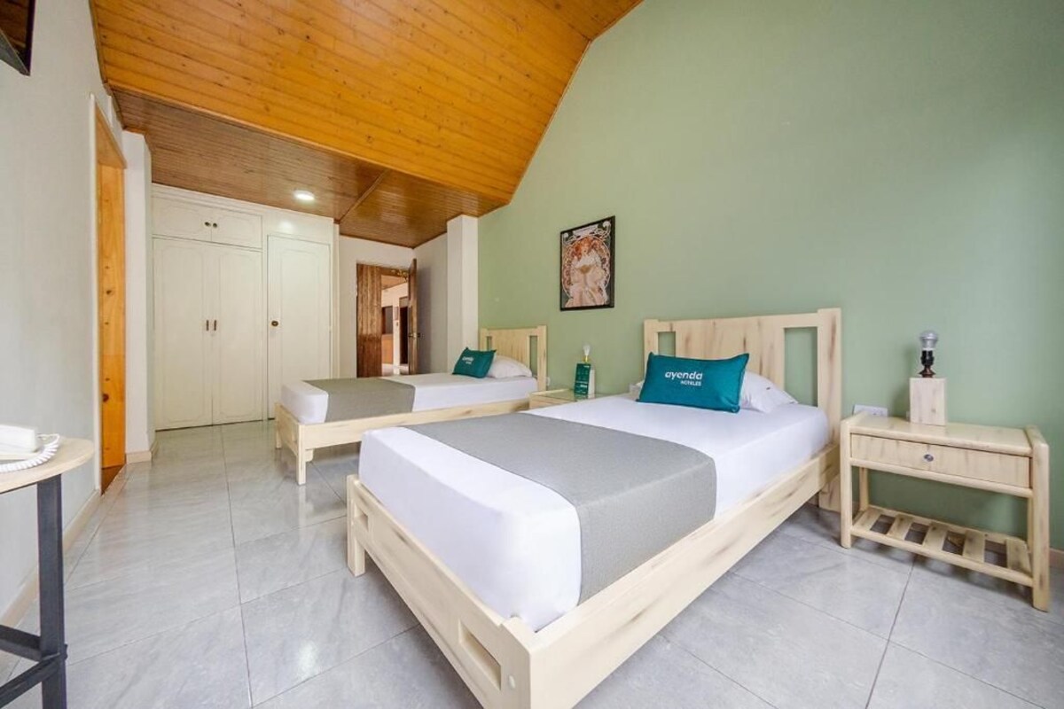 A bedroom with two beds, a wooden ceiling, and a green wall.