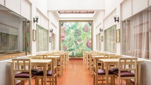 A dining hall with wooden tables and chairs arranged in rows, a large mural on the back wall, and large windows on the sides. - Ayenda Ana Carolina (Manizales)