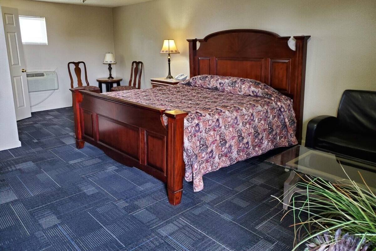 Una habitación de hotel con una cama de madera, una mesita, una silla y una lámpara.