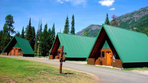 Una hilera de cabañas de madera con techos verdes, con montañas y árboles de fondo.