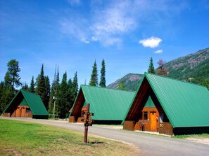 A row of log cabins with green roofs, set against a backdrop of mountains and trees. - Pahaska Tepee Resort (Cody)