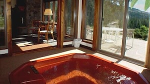 Una habitación con un gran ventanal que da a un patio exterior, una silla de madera y un jacuzzi.