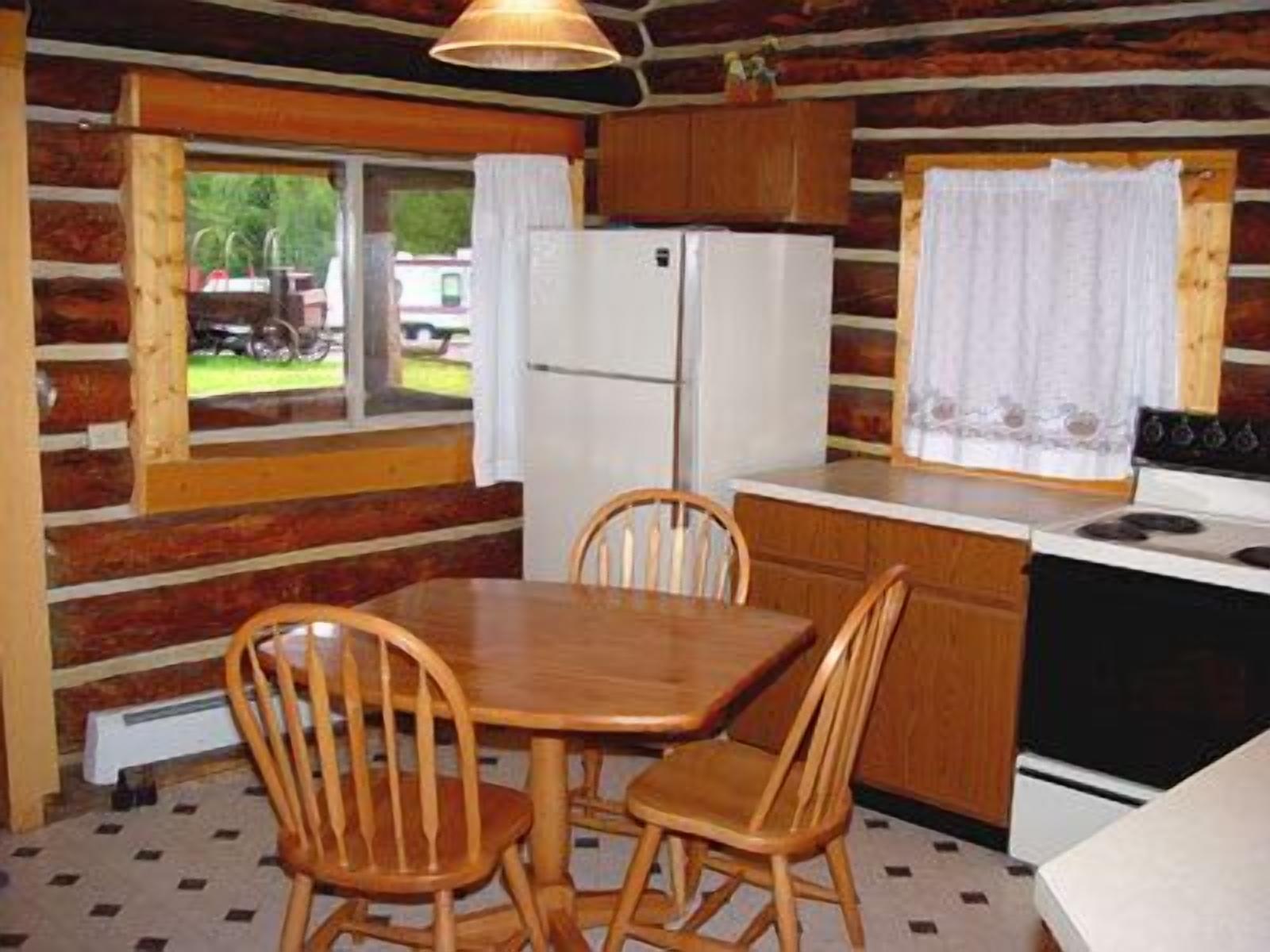 A compact kitchen with wooden cabinets, a refrigerator, a stove, and a dining table with chairs.