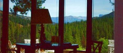 Une pièce dotée de grandes fenêtres donnant sur une forêt et des montagnes. Elle contient des tables et des chaises.