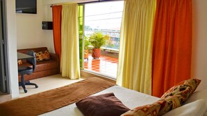 A hotel room with a bed, a sofa, a desk, and a potted plant by the window. - Hotel El Coliseo (Manizales)