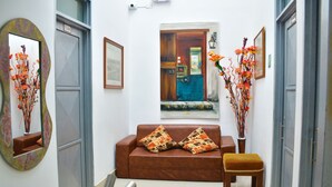 A hallway with a brown sofa, two matching cushions, a small wooden stool, a mirror with a floral frame, and a painting on the wall. - Hotel El Coliseo (Manizales)