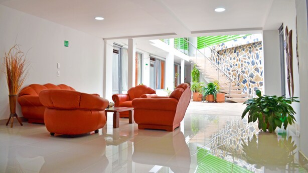 A spacious lobby with orange sofas, a coffee table, and potted plants. - Hotel El Coliseo (Manizales)