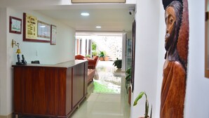 A hotel reception area with a wooden desk, framed certificates, and a large wooden sculpture. - Hotel El Coliseo (Manizales)
